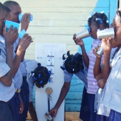 Haitianische Schulkinder in Uniform stehen beim Wasserrucksack Paul und trinken das gefiltere Wasser aus Bechern