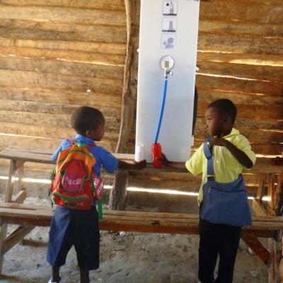 Zwei haitianische Schulkinder trinken von Paul, dem Wasserrucksack