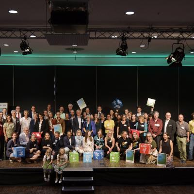 Gruppenfoto auf der Bühne der Volkshochschule Köln. Die Teilnehmenden halten farbige Würfel mit den Zielen für nachhaltige Entwicklung (SDGs) in den Händen.
