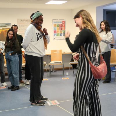 Eine Gruppe von Menschen steht im Kreis. In der Mitte des Kreises stehen zwei Personen, die zueinander gewannt sind und sich freuen erkennbar an einer freudigen Gestikulation.