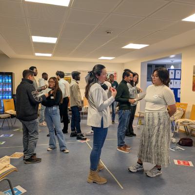 Eine Gruppe von Menschen steht in Zweier-Paaren in einem Raum und es wird sich unterhalten. 