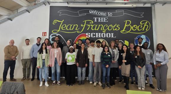 Eine Gruppe von Lehrkräften und internationalen Studierenden steht zusammen vor einer bunt bemalten Wand der Jeans Francois Boch Schule