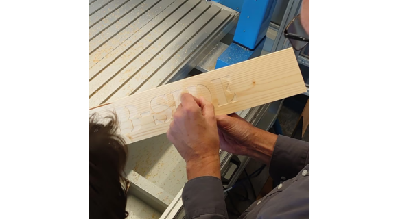Hände bearbeiten ein Stück Holz, auf diesem ist der Schriftzug "B-Side" eingeprägt