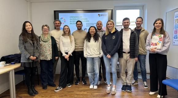Eine Gruppe von angehenden Lehrkräften, einer Studentin, zwei Mitarbeitenden des Studienseminars Neuwied und eine Grenzenlos-Projektreferentin stehen vor einer digitalen Tafel