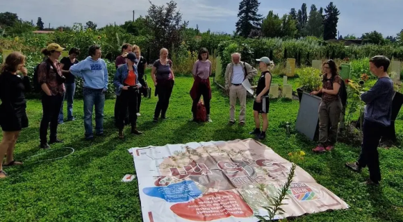 Bild zum Weltacker to go: Eine Gruppe von Erwachsenen steht auf einer Wiese und schaut ein großes Plakat auf dem Boden an.